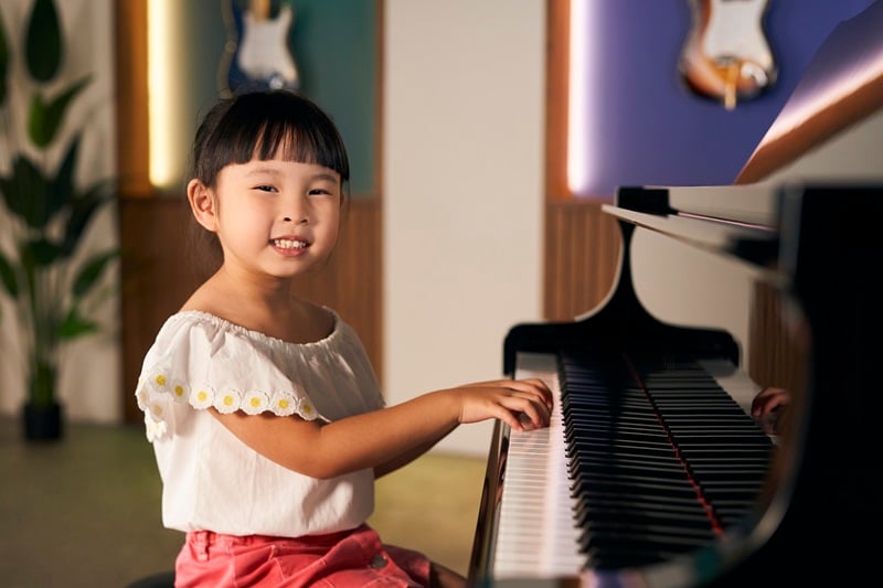 A young girl playing the piano while smiling happily into the camera.