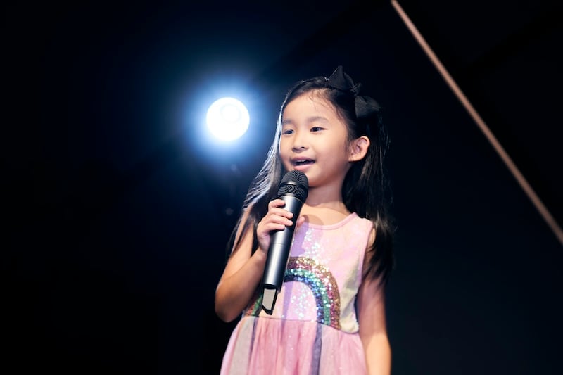 A young girl holding a microphone and happily singing.