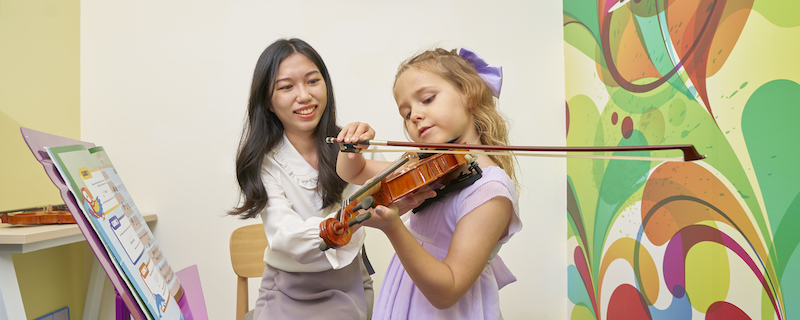 A teacher assisting her student, a young girl, on how to properly hold a violin during a lesson.