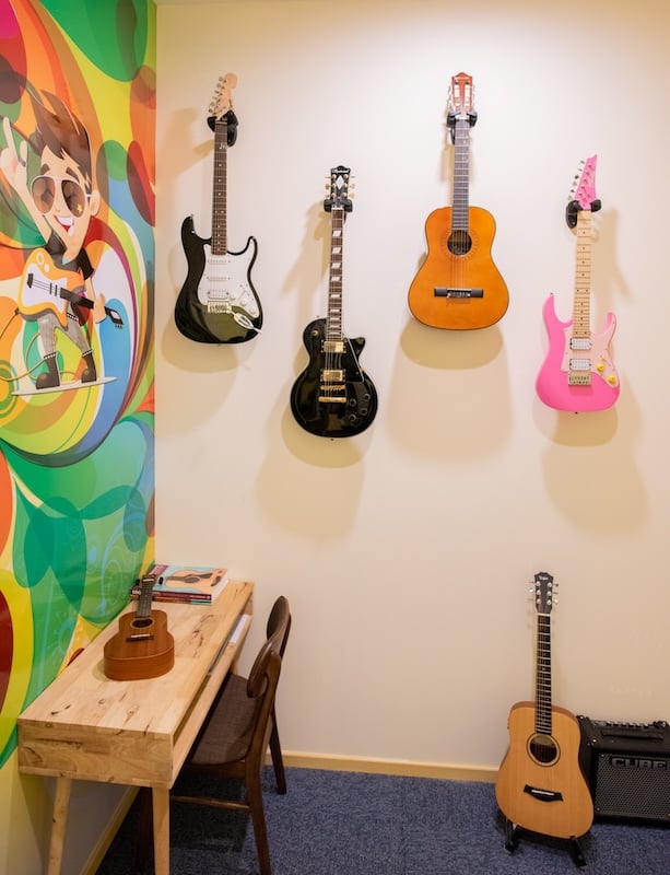 A music school studio with a number of guitars and ukuleles ranging from electric, to classical and even a hot pink edition!